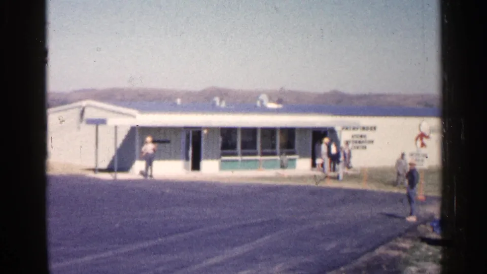 Low white Pathfinder visitor center in Sioux Falls, South Dakota, with people gathered near the entrance in 1960 8mm footage.