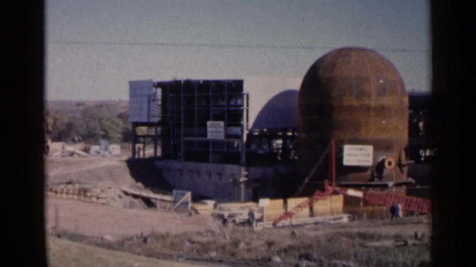 1960 Sioux Falls 8mm frame showing a rust-colored dome-shaped structure, scaffolding, signs, and construction materials outdoors.