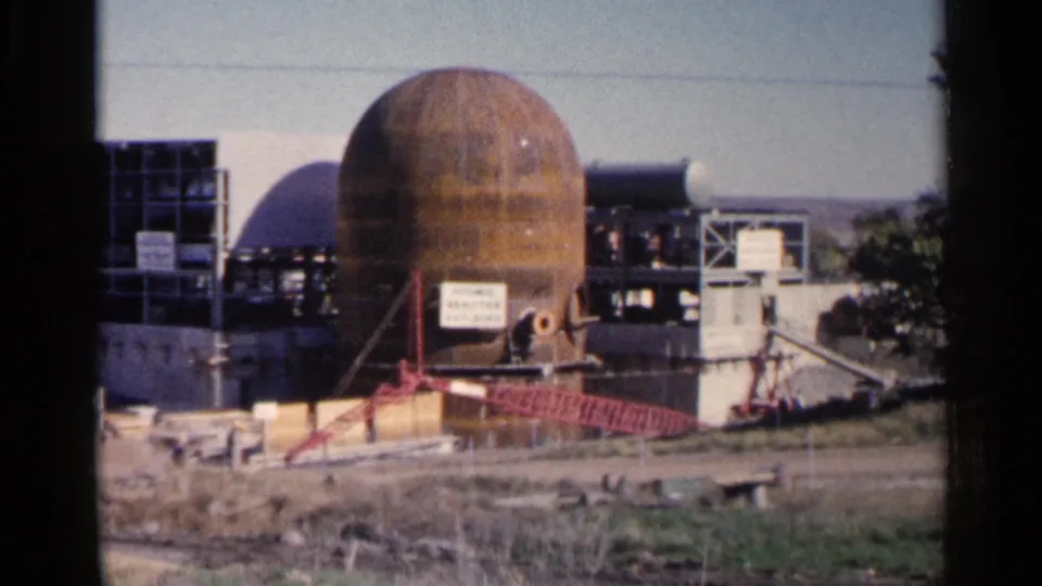 1960 Sioux Falls 8mm view of the rust-colored dome, red crane arm, scaffolded sections, and scrubby foreground vegetation.