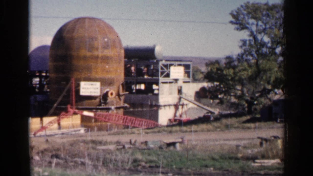 Rusted dome structure and work-site equipment beside a tree and open road.