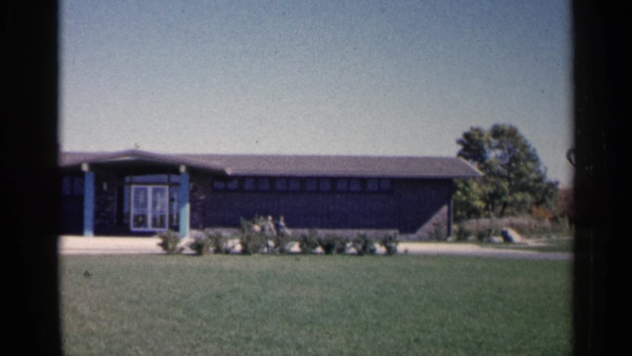 Low modern visitor center building across a lawn under a clear sky.