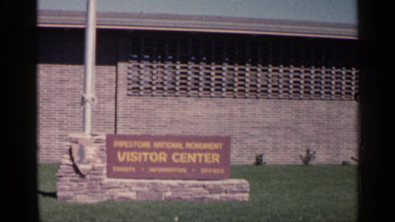 Visitor center sign beside a brick building and flagpole.