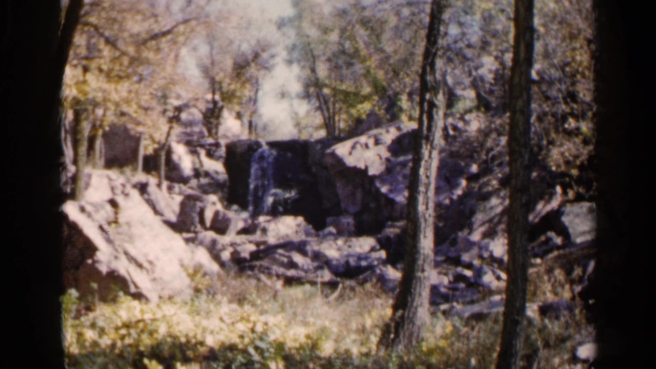 Rocky waterfall framed by trees, with a seated adult near the right edge.