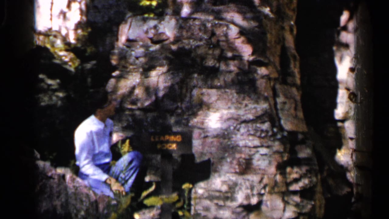 Man seated beside a Leaping Rock sign and large boulders under trees.