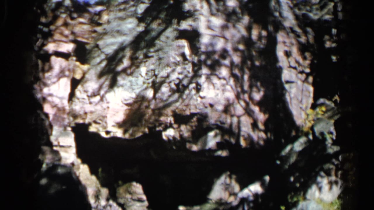 Dark cave opening looking toward sunlit rock with tree shadows.