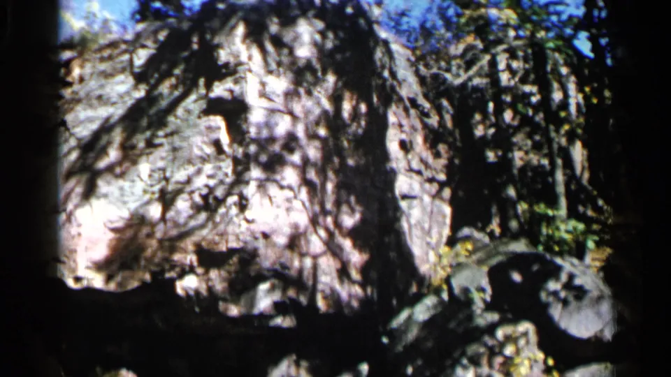 1960 8mm frame from Sioux Falls showing a cave-framed view of pale rock, dark foreground shadow, and leaves at the right edge.