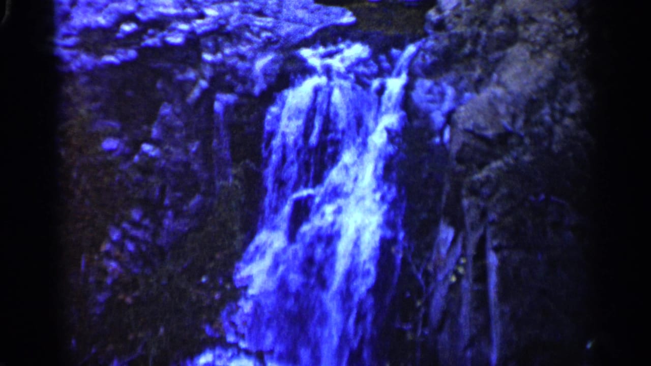 Blue-toned waterfall cascading over dark rocks with black film borders.