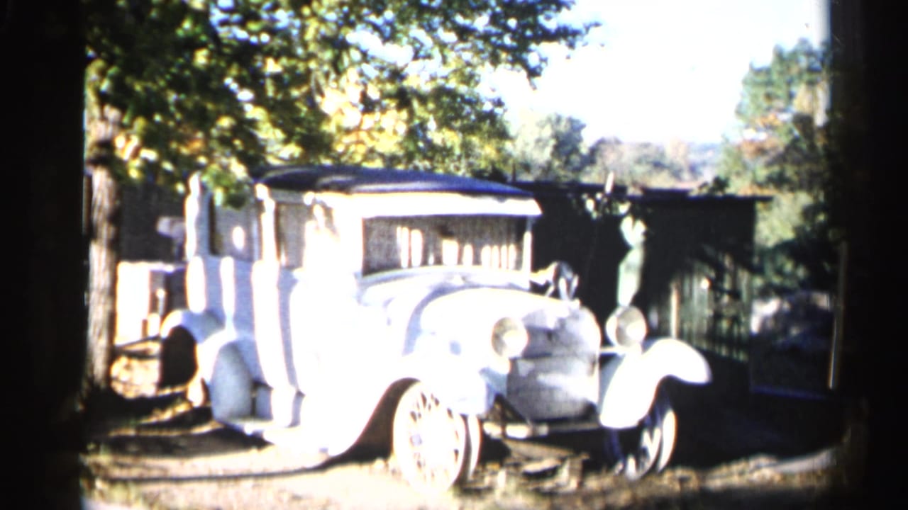 1960 Sioux Falls 8mm frame showing a light-colored antique car with large fenders parked in a shaded outdoor area.