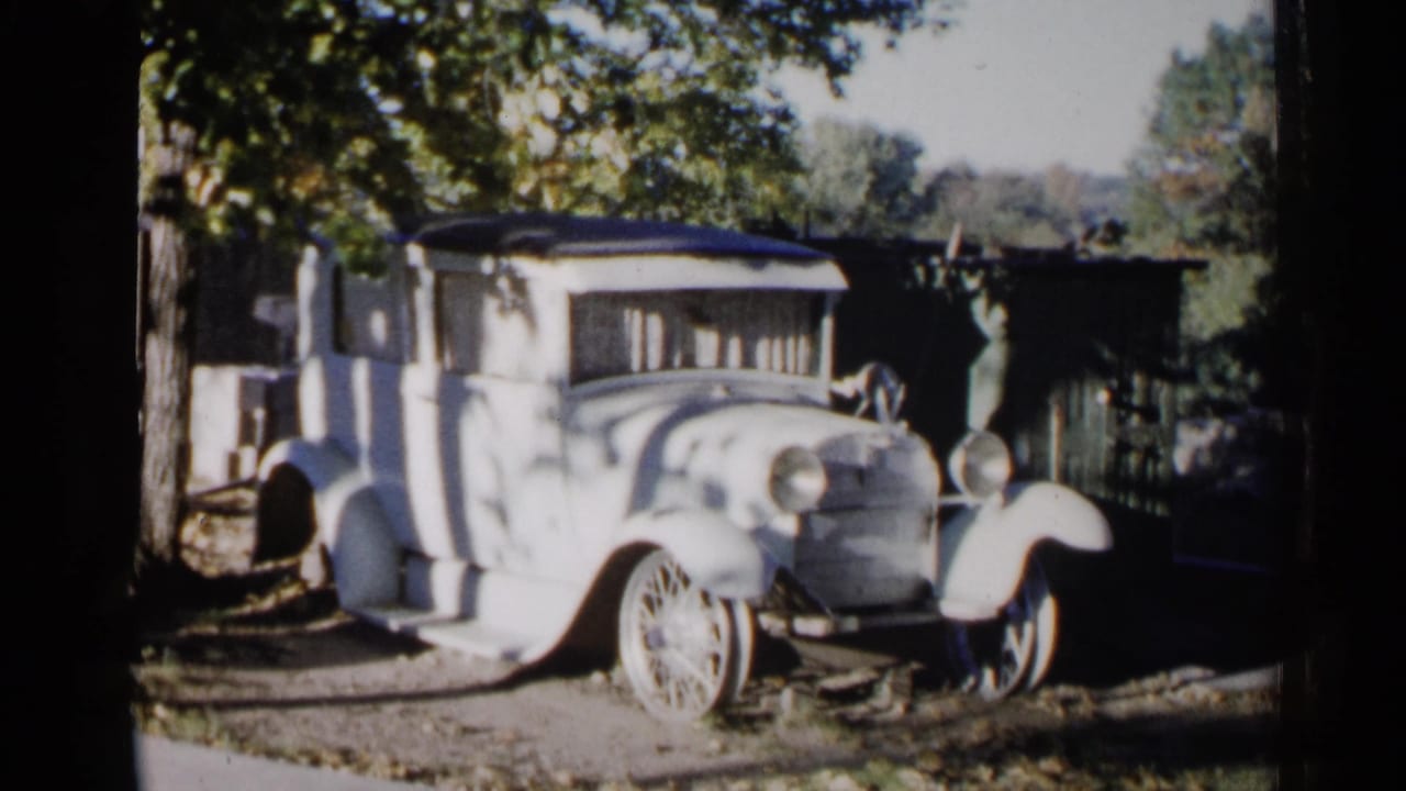 Antique car beside trees and a dark fence or structure.