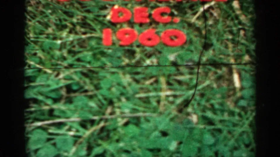 A cropped 8mm frame shows DEC. 1960 in red plastic letters on grass, with visible film wear and soft focus.