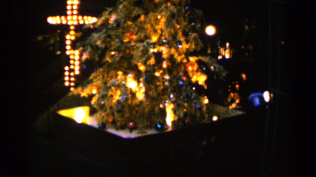 1960 Sioux Falls home-movie frame showing a glowing Christmas tree and illuminated cross against a dark background.