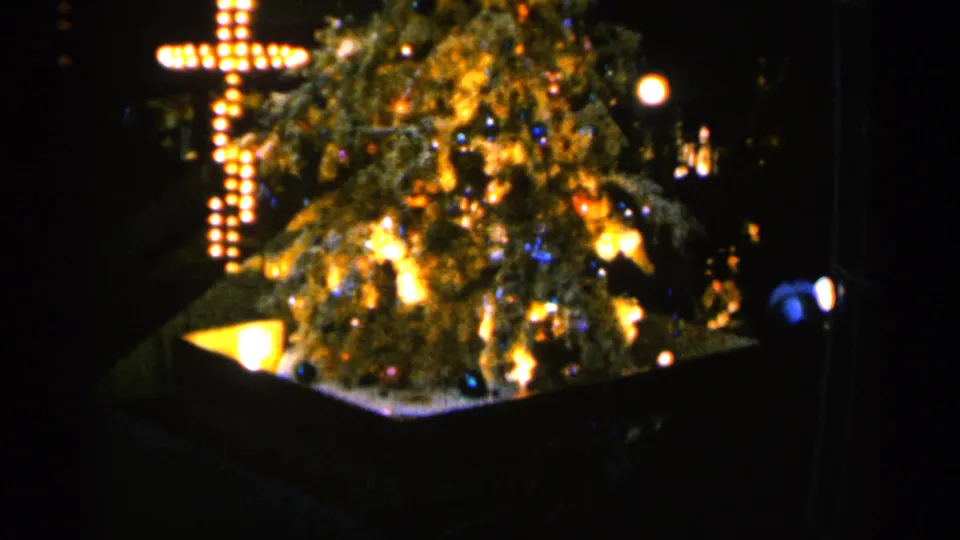 1960 Sioux Falls 8mm frame showing a decorated Christmas tree and bright bulb-lit cross in a dark holiday scene.