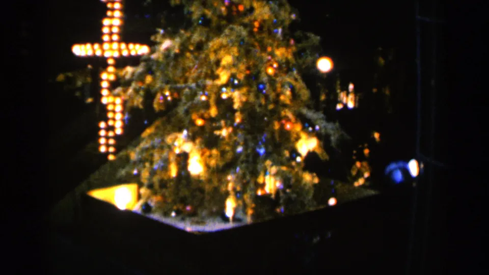 Final 1960 Sioux Falls frame of the nighttime Christmas display, with the lit cross and tree softened by 8mm grain.