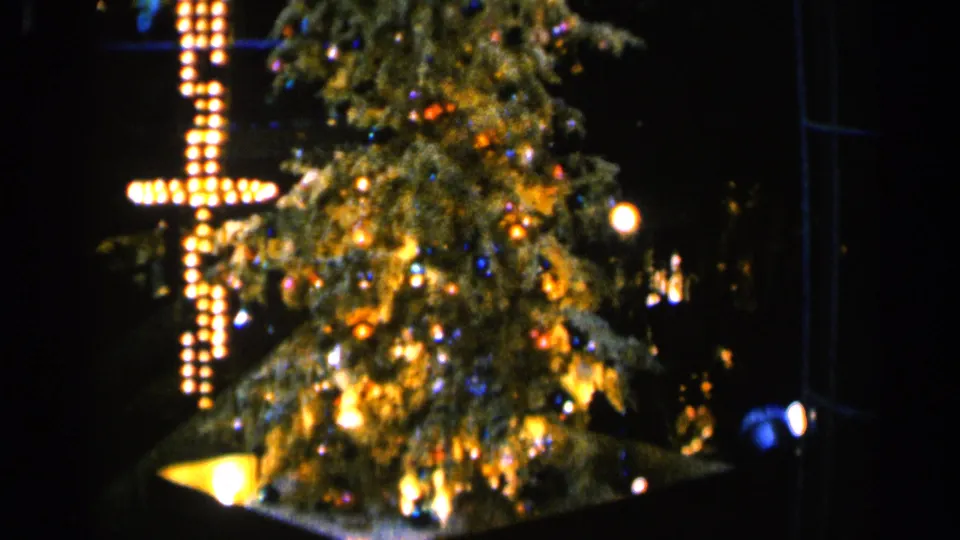 1960 Sioux Falls holiday frame with a brightly lit Christmas tree and cross-shaped bulb display, softened by 8mm focus and grain.