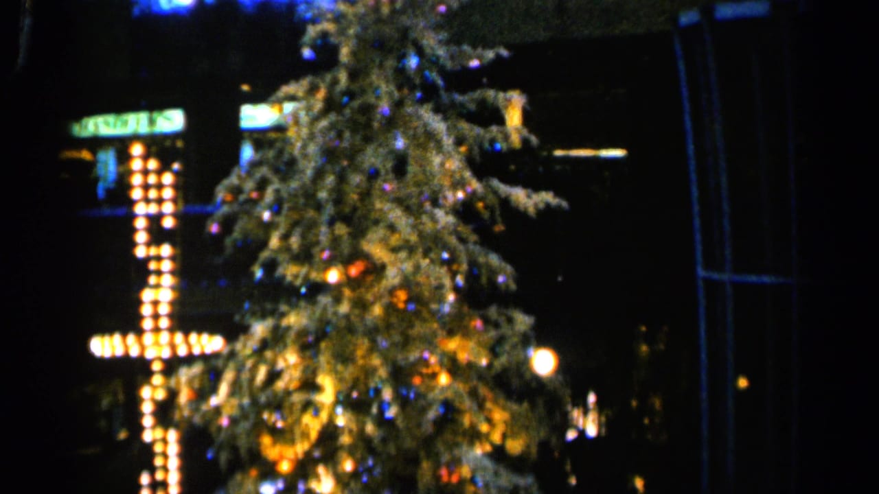 Decorated Christmas tree at night beside a bright cross-shaped light display.
