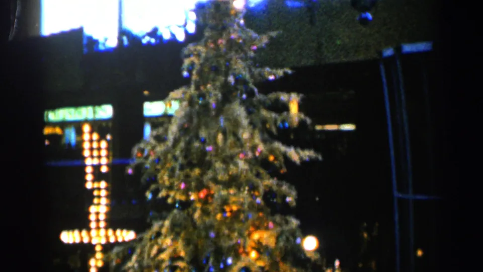 Vintage 8mm frame from Sioux Falls in 1960 showing a decorated outdoor Christmas tree and adjacent cross-shaped holiday lights.