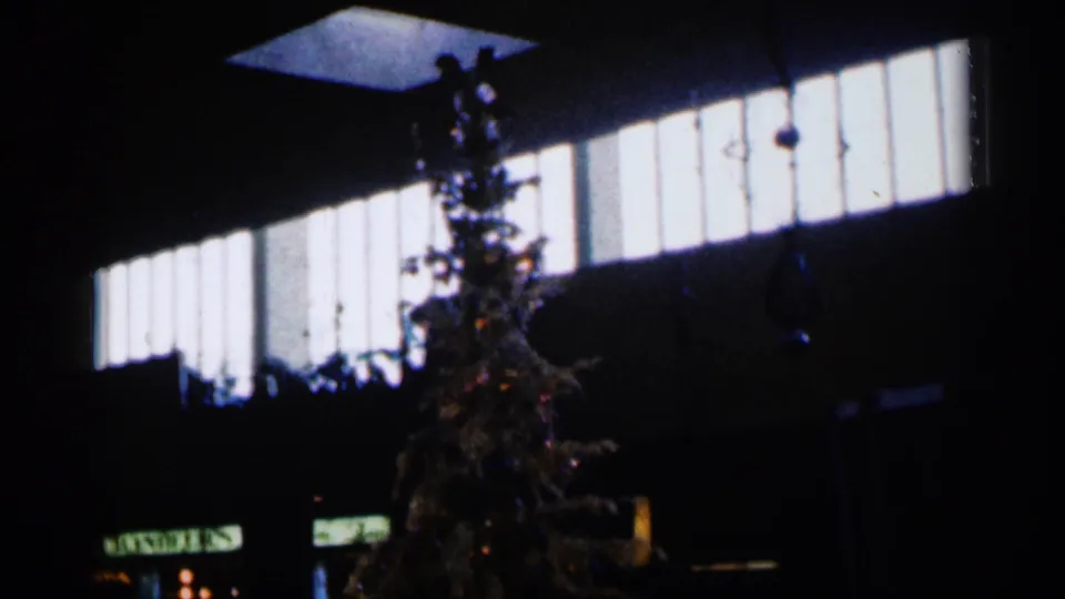 1960 Sioux Falls 8mm frame showing the holiday tree darker in the frame, with high windows and hanging decorations above.