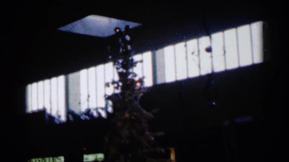 1960 Sioux Falls home-movie frame showing a Christmas tree in a dark interior beneath a bright rectangular window.