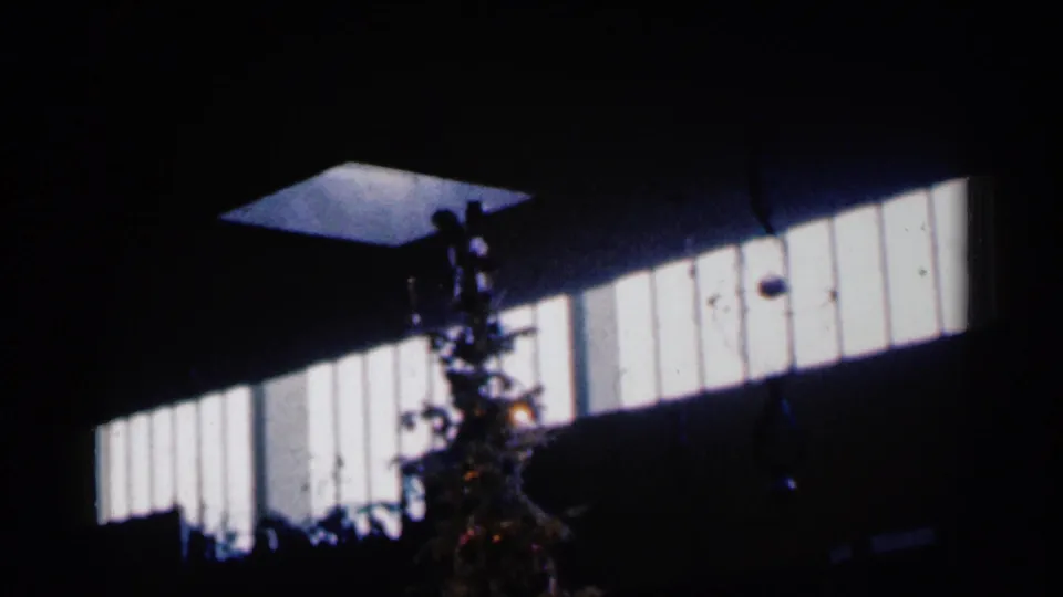The decorated tree appears in silhouette with high-contrast window light behind it in the 1960 home-movie frame.
