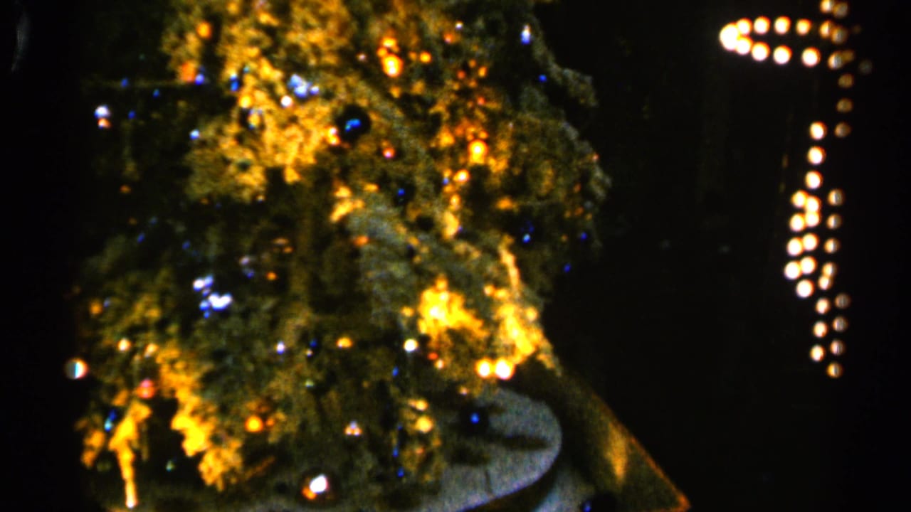 Decorated Christmas tree with glowing colored lights in a dark room.