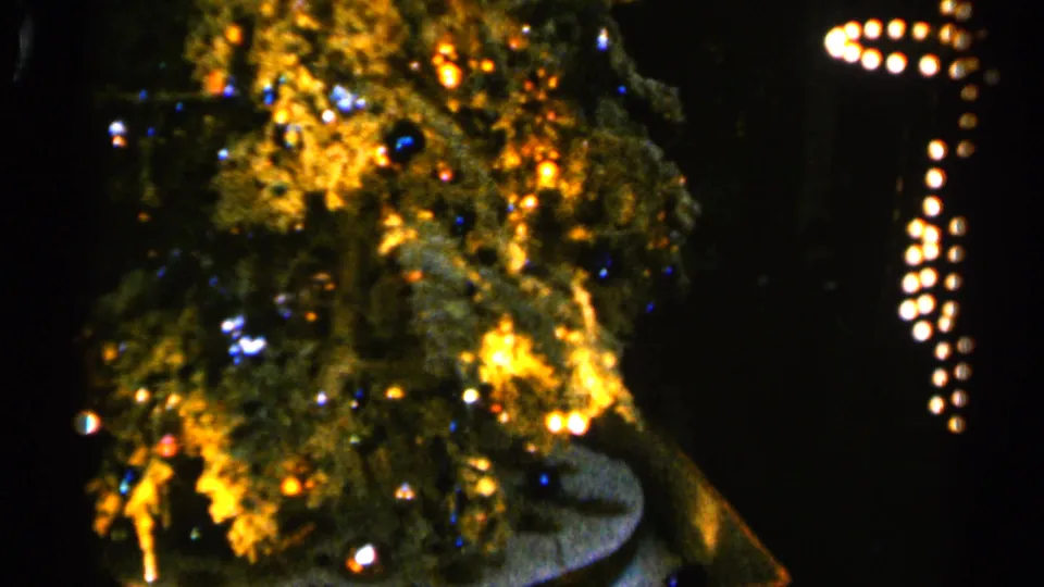 1960 Sioux Falls home-movie frame of a lit Christmas tree with warm bulbs, ornaments, and a dark surrounding interior.