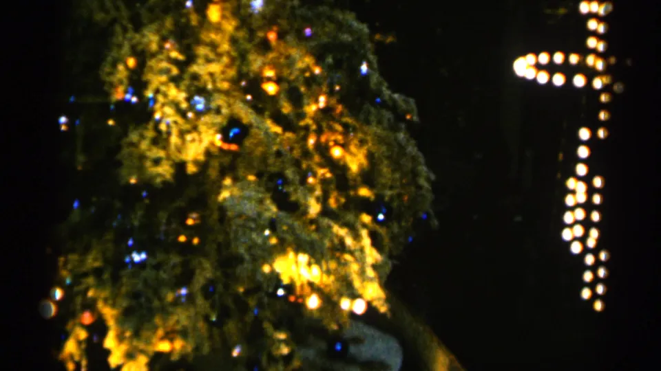1960 Sioux Falls frame showing the rotating Christmas tree shifted beside a vertical holiday light pattern in darkness.