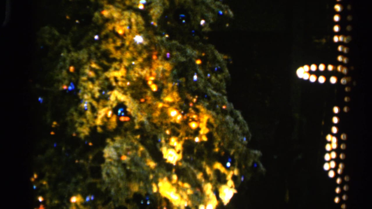 1960 Sioux Falls 8mm frame showing a lit Christmas tree with warm bulbs, blue points of light, and a vertical light strand at right.
