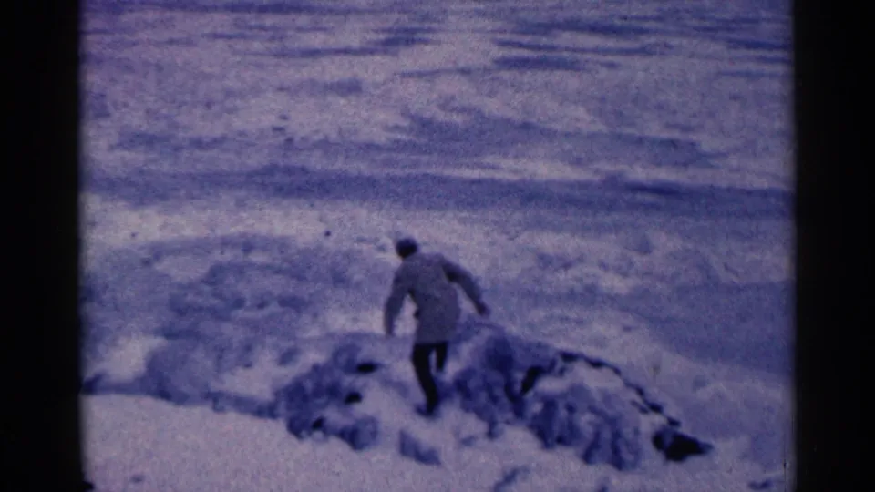 In the Duluth winter scene, a distant adult in a coat and hat walks across snow near a darker open area.