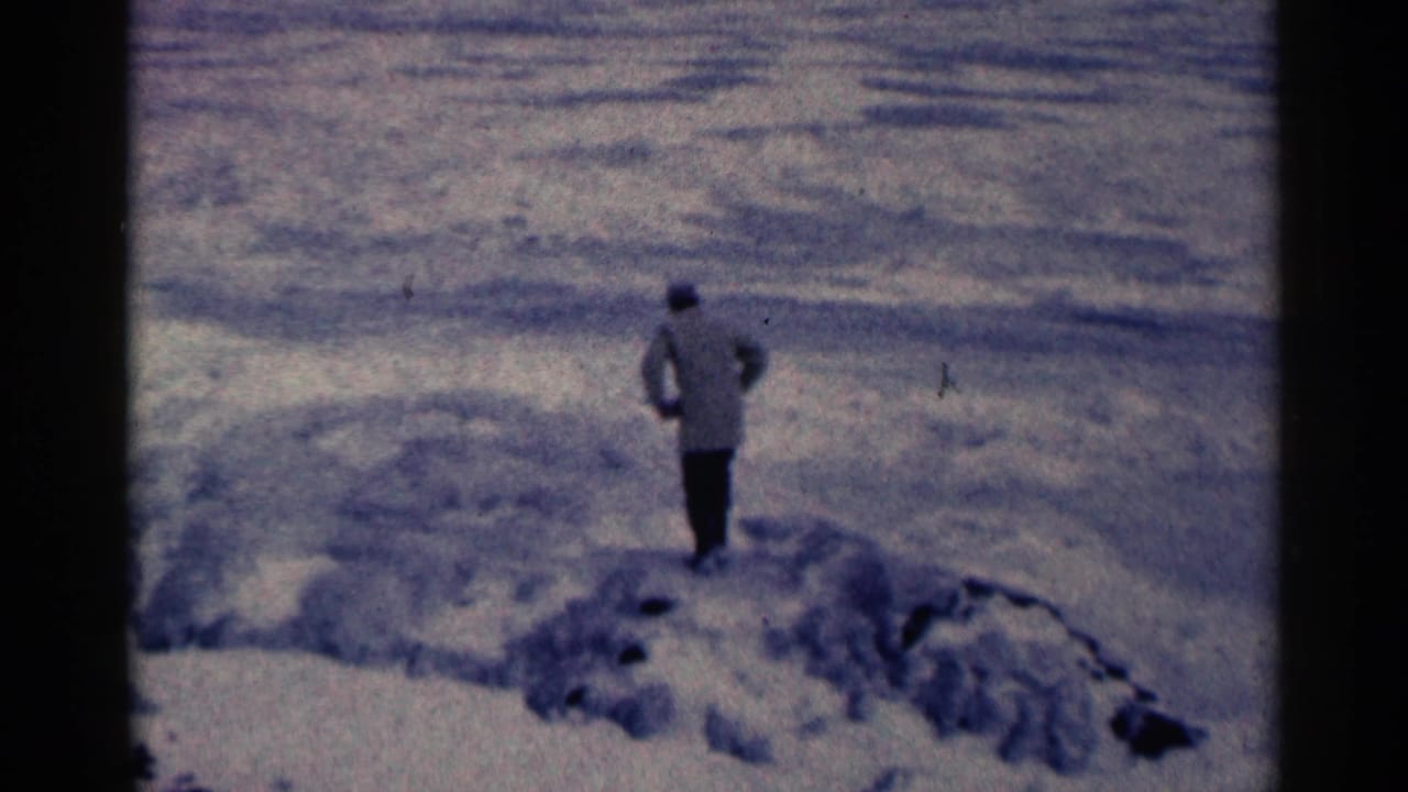Bundled man standing on snowy, uneven ground near dark rocks.