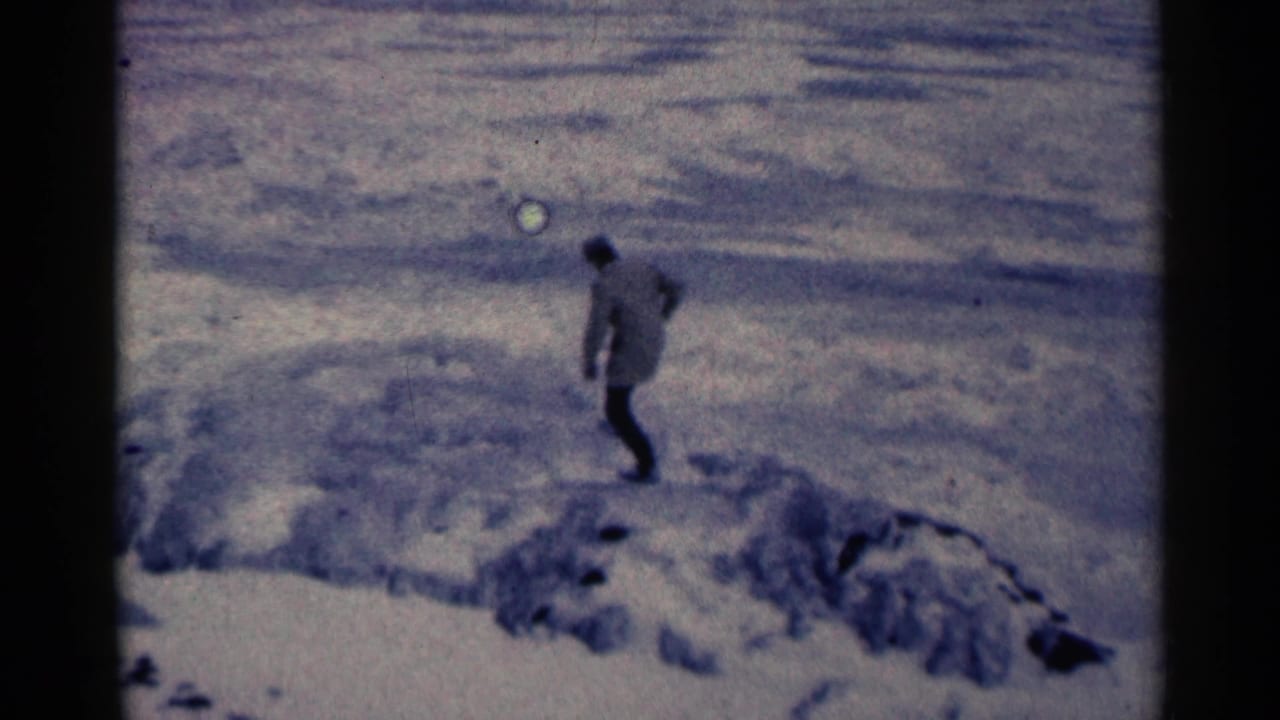 Man in winter clothing steps across snow beside icy ridges.