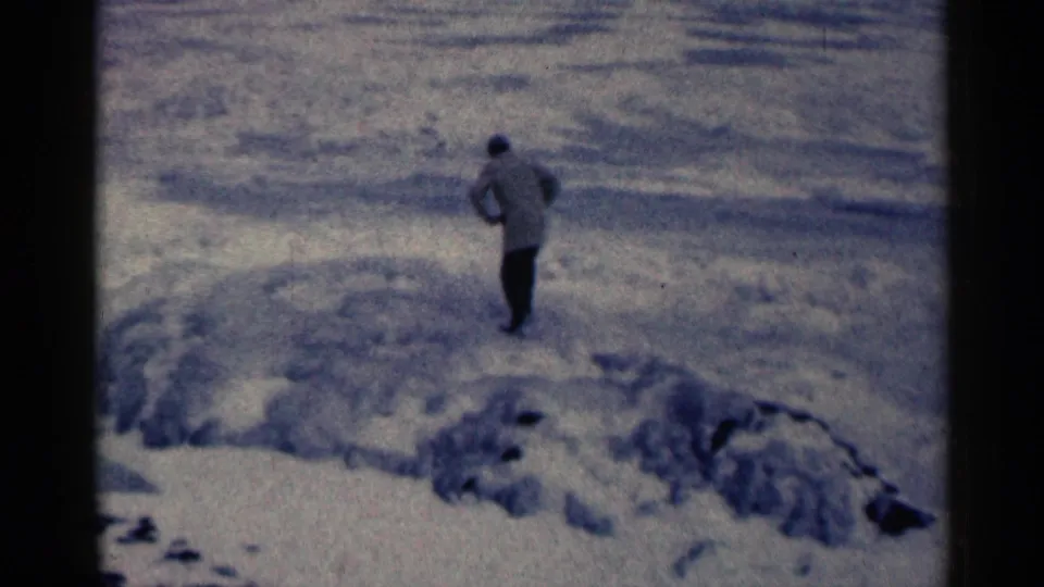 The figure continues across the snow-covered terrain, framed by a cold blue cast and handheld 8mm home-movie texture.