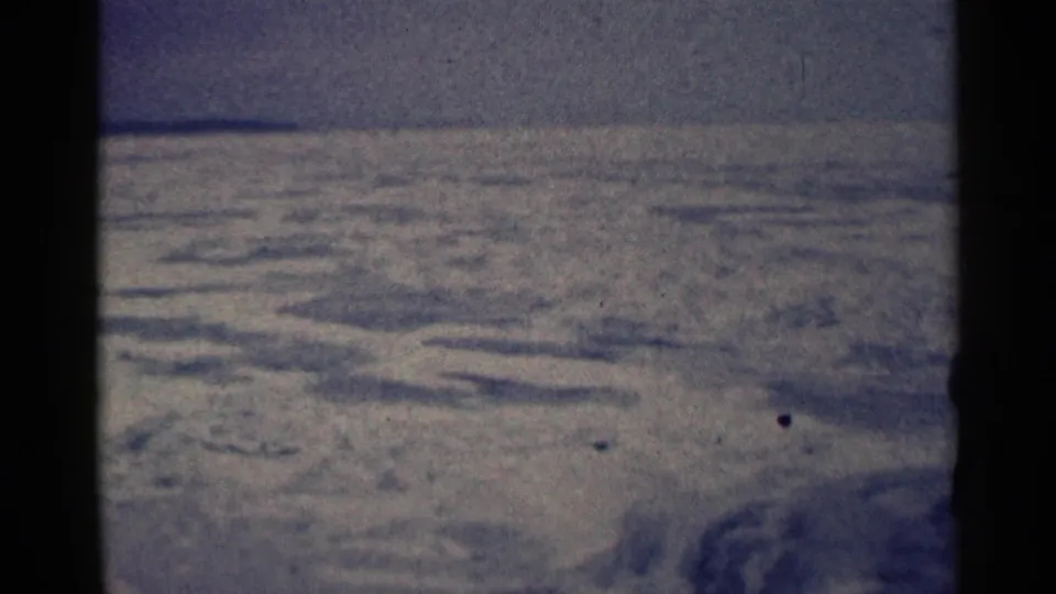 1961 Duluth home-movie frame showing open snowy terrain, low mounds, a flat horizon, and dark film-edge borders.
