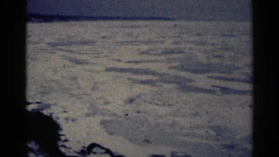 1961 Duluth winter terrain seen through 8mm frame edges, with snow mounds, soft grain, and a subdued sky.
