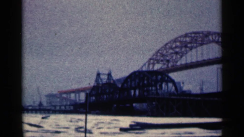 1961 Duluth home-movie view of the arched bridge structure, dark truss span and gray water below.