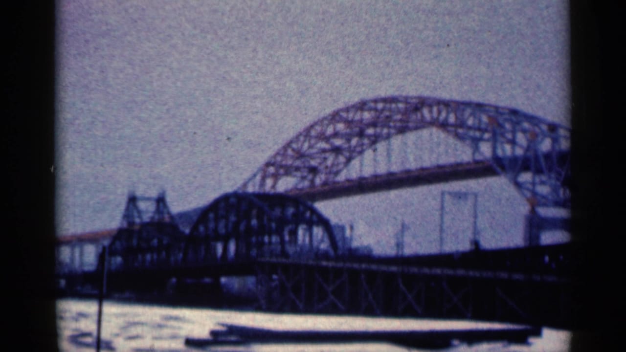 The Duluth bridge span fills the frame, with arched steel lattice above river water and a faint distant tower.