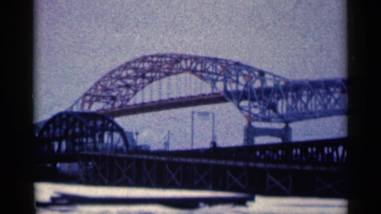 Steel arch bridge seen beyond a darker foreground truss over water.