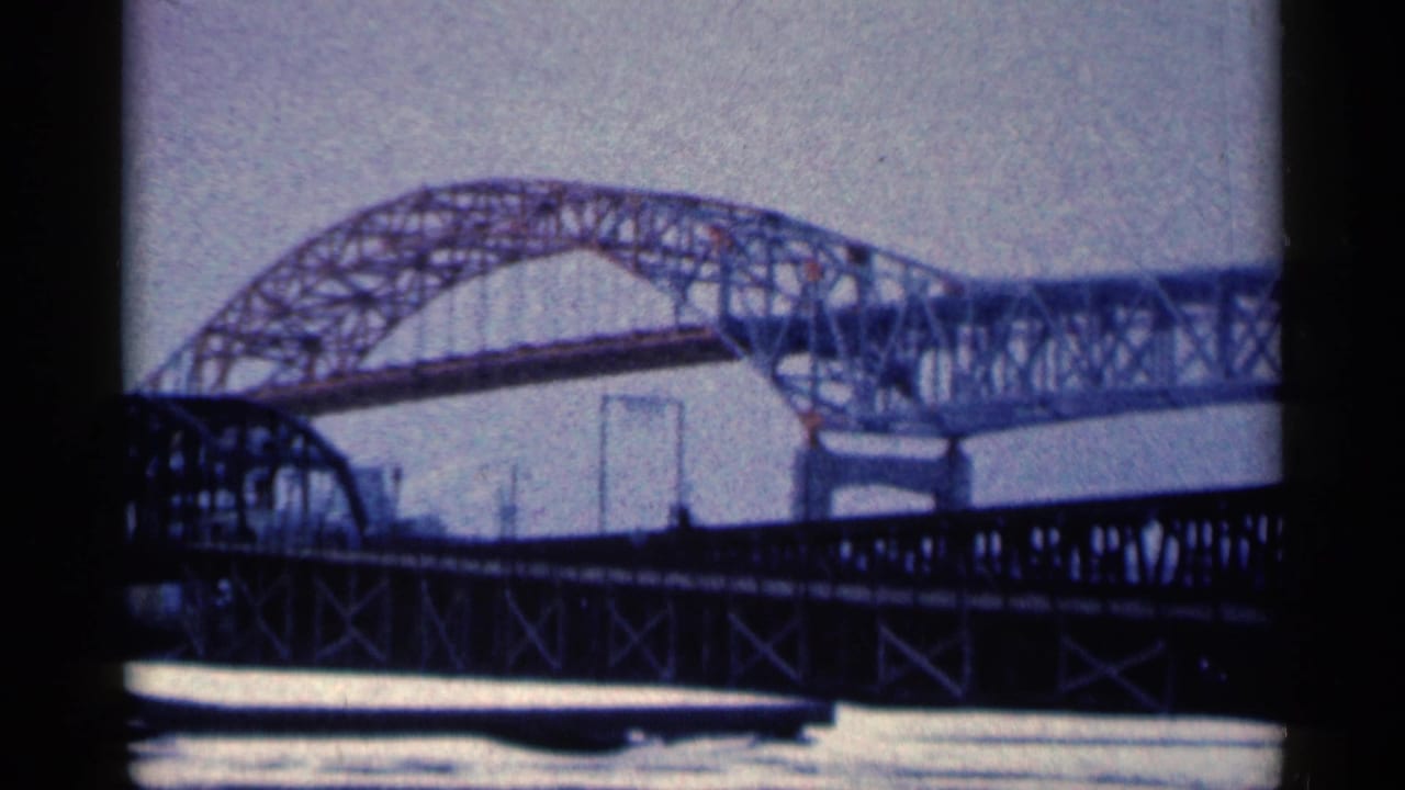 Large steel arch bridge spans the frame above a dark truss bridge.
