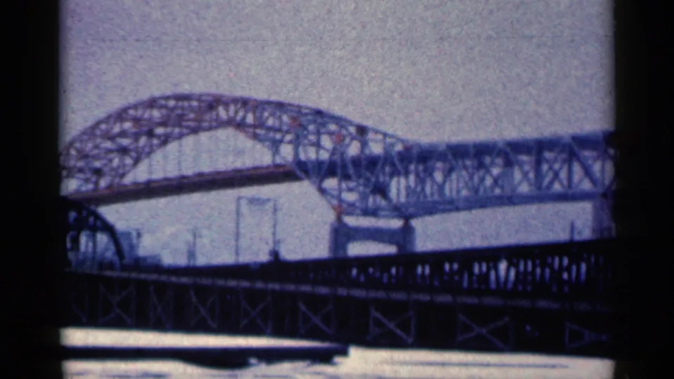 1961 Duluth frame showing the bridge's lattice steelwork, foreground truss, water, and pale sky in soft 8mm color.