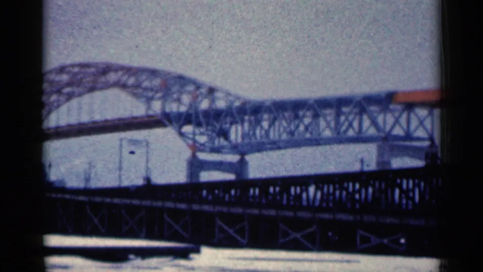 Blue-shifted 8mm frame of the Duluth steel bridge seen behind a darker truss bridge, with visible film gate borders.