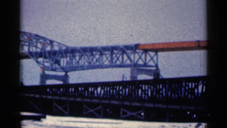 Steady 8mm frame from Duluth showing a dark lower bridge structure, water, and a lighter metal bridge crossing the background.