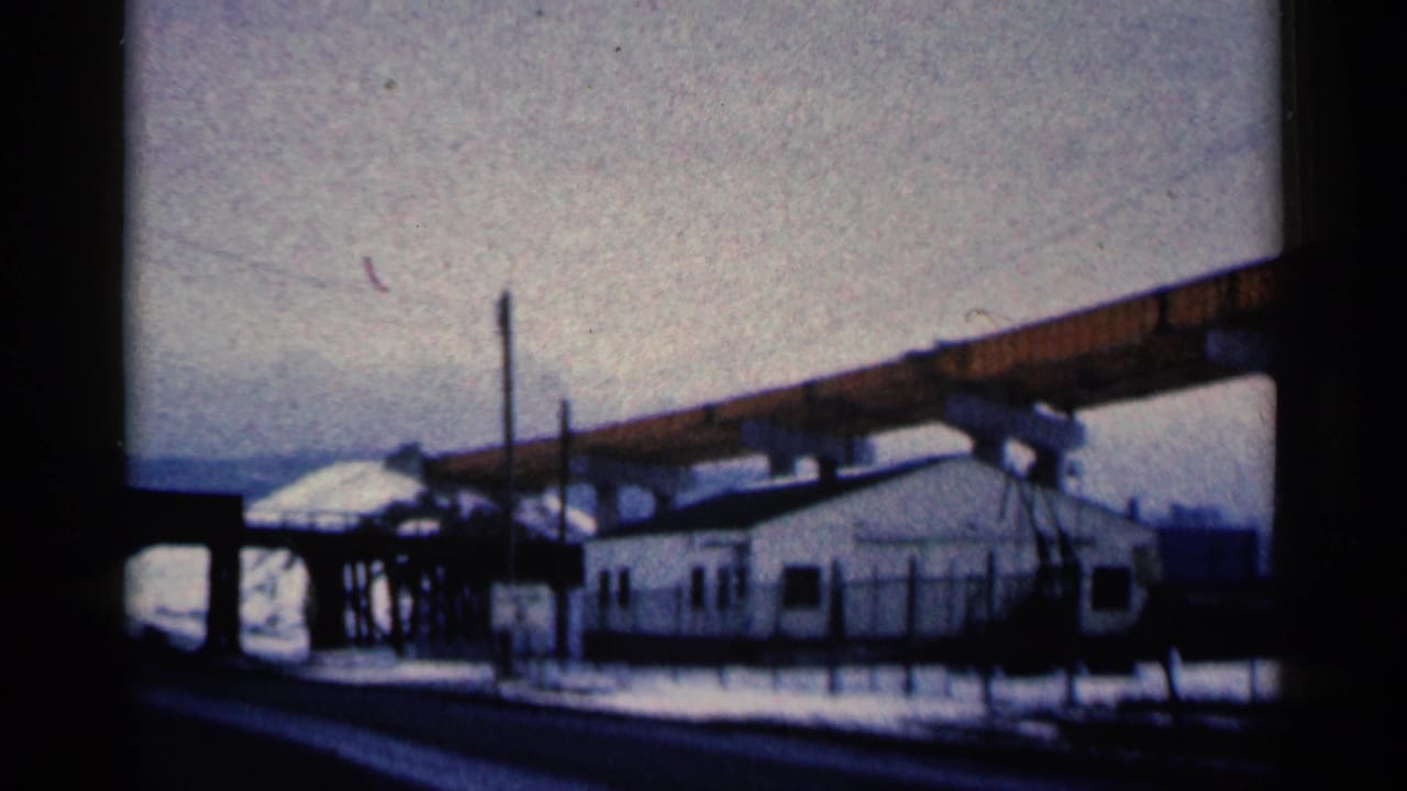 White fenced building beneath an elevated orange beam in a snowy industrial area.