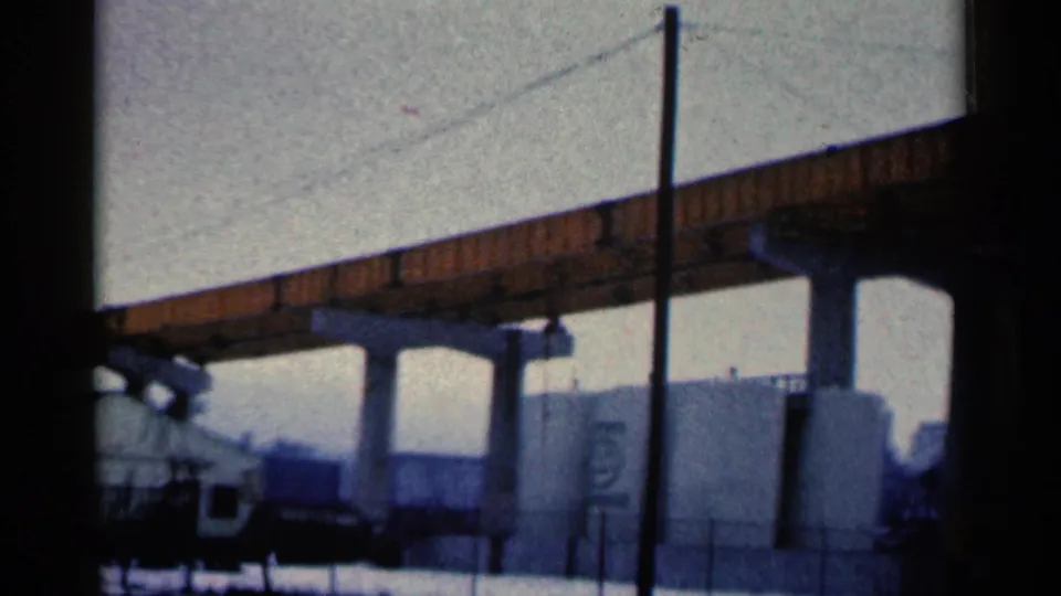 End frame from 1961 Duluth footage with an elevated orange bridge, a vertical pole, gray tanks, snow, and a partial white building.