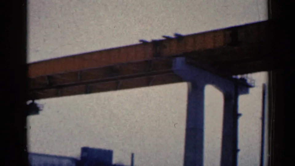 Final 1961 Duluth frame showing a concrete bridge pier, orange span, utility poles and low industrial forms beneath a hazy sky.