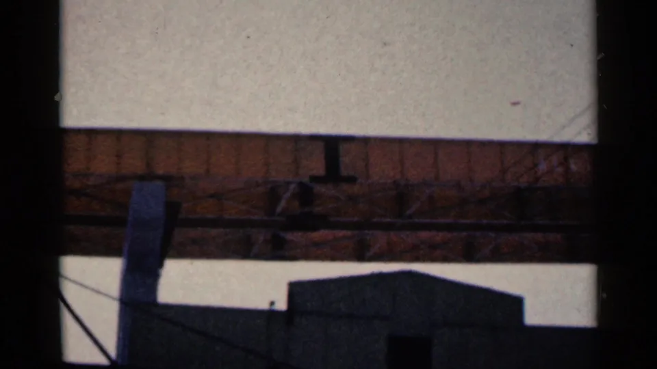 1961 Duluth frame with a railroad bridge span crossing above a silhouetted industrial building and utility lines.