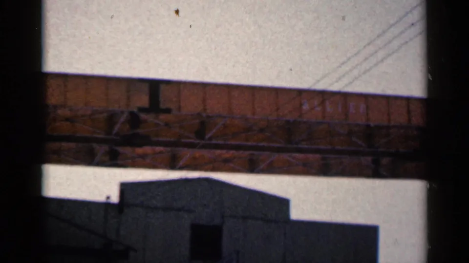 1961 Duluth 8mm frame showing bridge trusswork, diagonal power lines, and the upper portion of a dark industrial building.