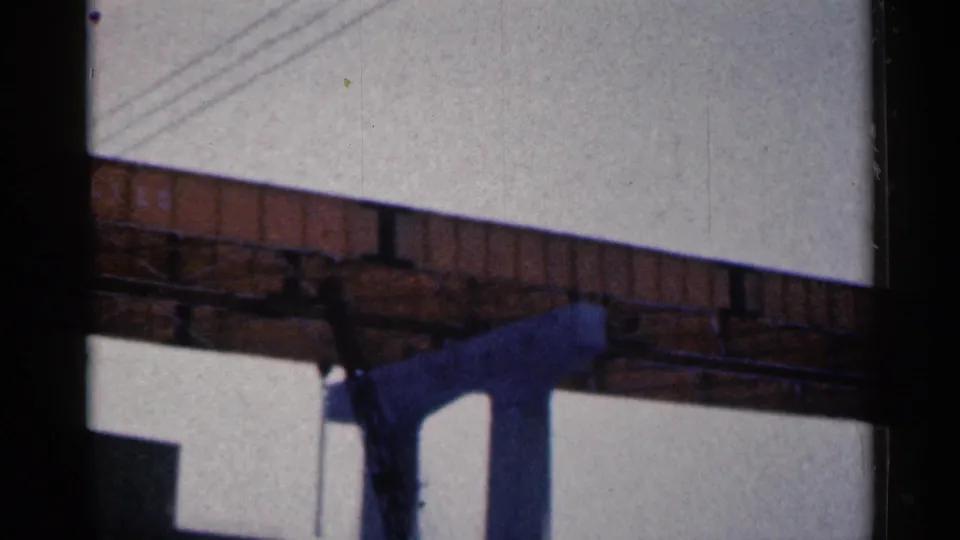 1961 Duluth home-movie view of the bridge underside and blue support column, with diagonal utility lines and a low building corner beneath.