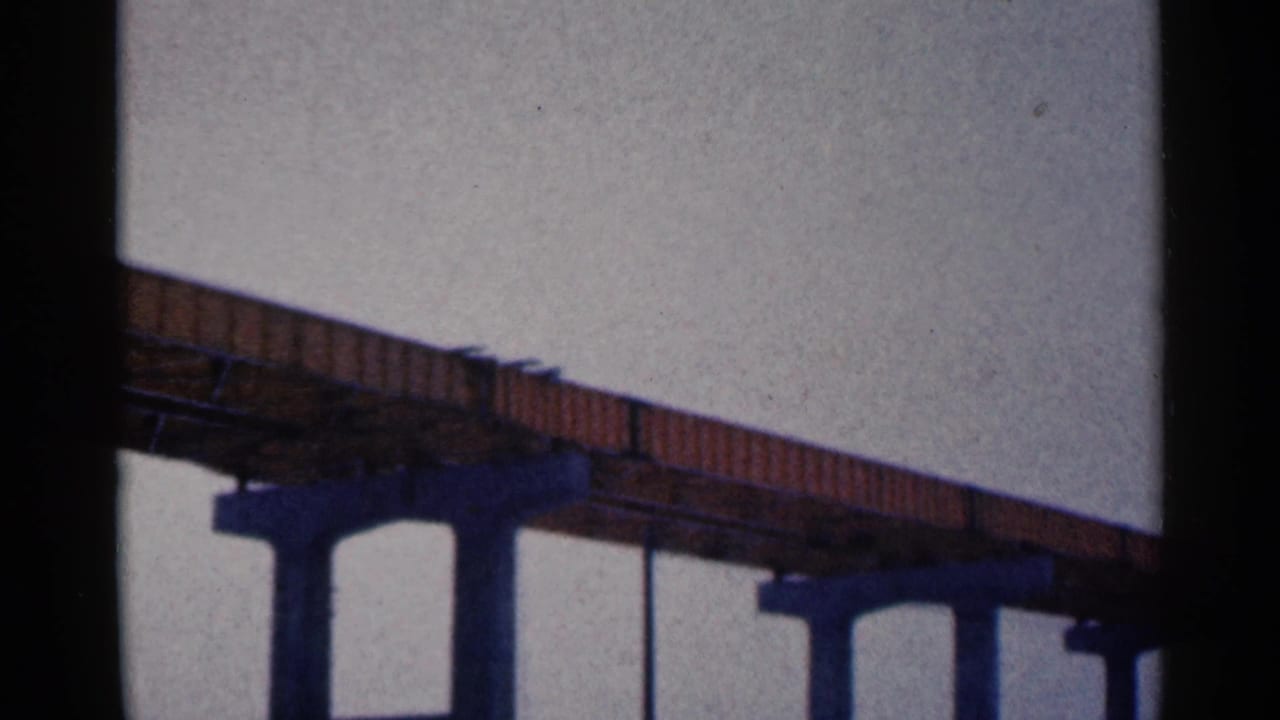 Low-angle view of a steel bridge deck on concrete pilings against a pale sky.