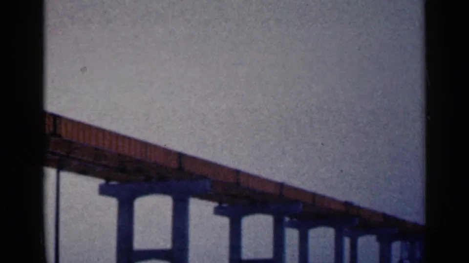 1961 Duluth archival frame showing a steel bridge structure on concrete pilings, with muted 8mm color and grain.