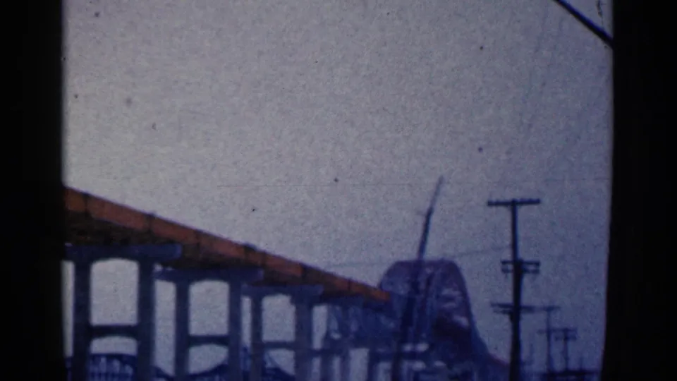 1961 Duluth home-movie view of bridge supports, roadside utility poles, and a distant arched bridge form.