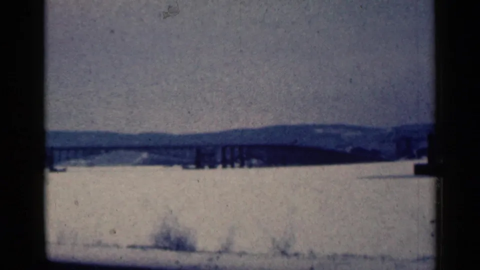 1961 Duluth, Minnesota home-movie frame showing a long bridge over frozen water, with snow and brush in the foreground.